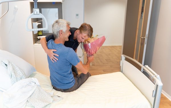 Patiënt wordt uit bed geholpen door familielid of bekende
