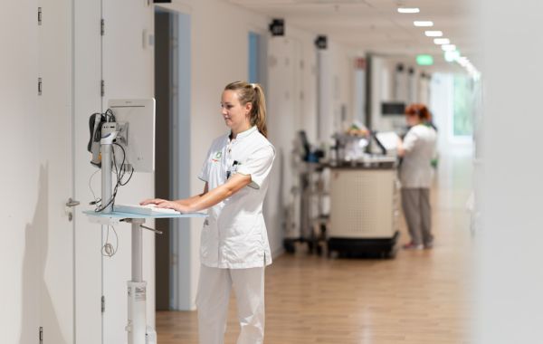 Verpleegkundige in ziekenhuisgang achter registratiescherm