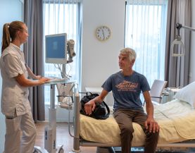 Verpleegkundige achter monitor spreekt met patiënt